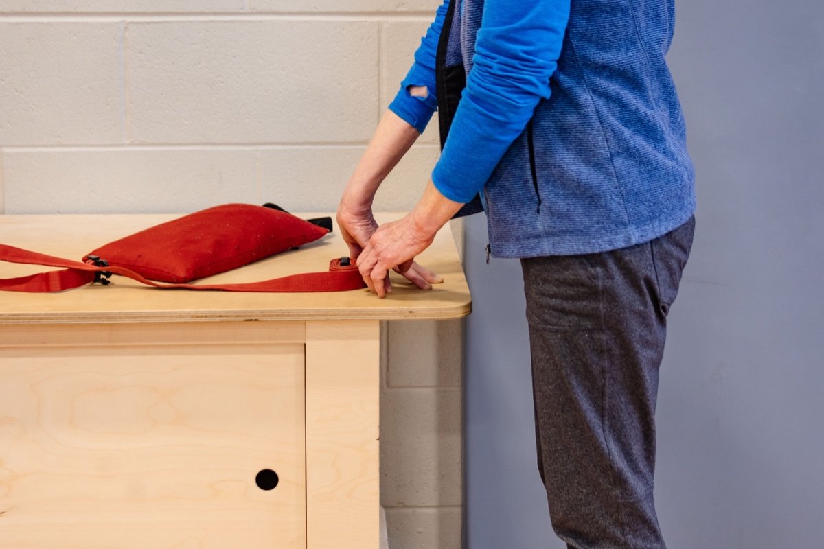 An older student standing fully dressed at a table, working her hands, nobody on the floor