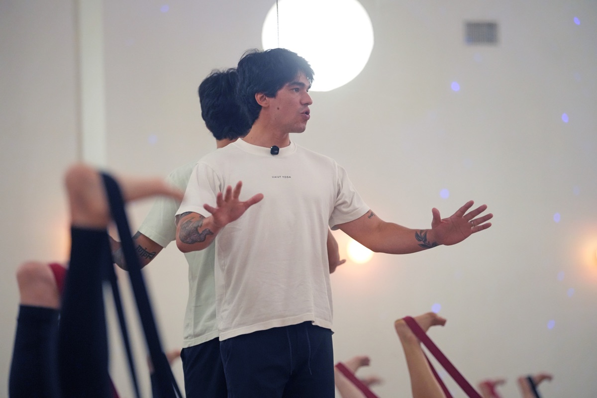 Ravi Kaiut teaching, hands open mid-explanation, students working with straps in the foreground